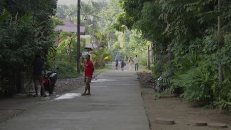 Rural-village-road-in-the-Philippines-with-locals,-some-walking-and-a-parked-motorcycle