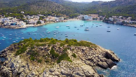 Playa-de-san-telmo-beach,-with-clear-blue-waters-and-anchored-boats,-aerial-view,-on-the-island-of-Mallorca,-Spain,-in-the-Mediterranean-Sea
