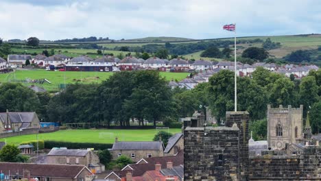 Drone-Shot-of-British-Flag-Waving-on-Top-of-Alnwick-Castle-Tower,-England-UK-60fps