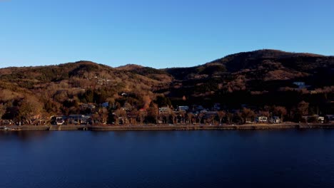 A-serene-lakeside-town-at-dusk,-with-hills-in-the-background-and-clear-skies,-aerial-view