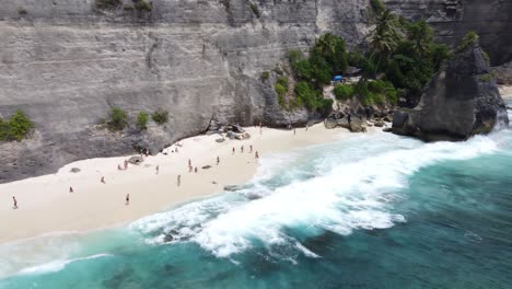 Gente-En-La-Playa-De-Arena-Blanca-De-Diamantes-Respaldada-Por-Acantilados-De-Piedra-Caliza,-Nusa-Penida,-Aérea