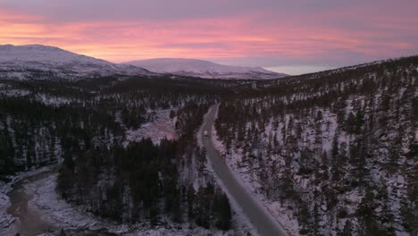 Twilight-hues-over-snowy-Norwegian-landscape-with-a-lone-truck-on-road,-aerial-view