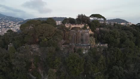 Waterfall-on-Top-of-a-Hill-in-French-Riviera-Next-to-Vegetation-and-City-of-Nice,-Mediterranean-Sea
