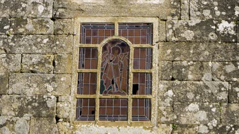 Stained-glass-window-showing-wanderer-in-humble-clothes-set-in-stone-wall-facade