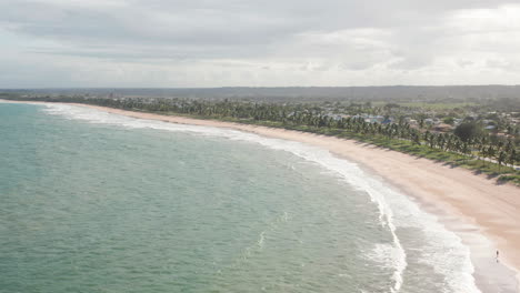 Aerial-view-of-the-beach,-large-green-area-with-palm-trees-and-some-people-walking,-Guarajuba,-Bahia,-Brazil