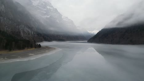 Klöntalersee-Glarus-Switzerland-low-flight-over-amazing-frozen-lake-with-misty-clouds