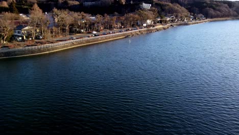 Lakeside-town-during-sunset-with-trees-casting-long-shadows,-aerial-view