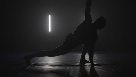 male-athlete-doing-yoga-stretches-as-workout-warming-up-in-black-and-white-studio,-silhouette-yoga