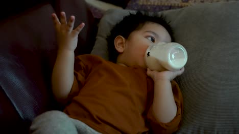 Niño-Con-Camisa-Naranja-Acostado-Bebiendo-De-Una-Botella,-Centrado-En-La-Pantalla-Del-Televisor,-En-El-Interior