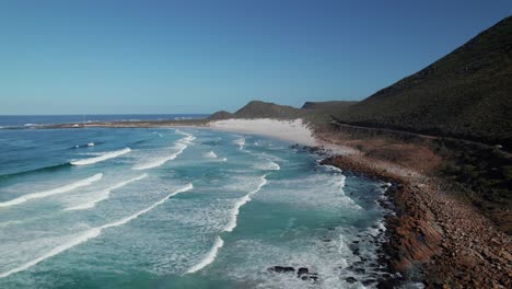 Foamy-Ocean-Waves-Splashing-On-Rocky-Shore-Of-The-Beach-In-Misty-Cliffs,-Cape-Town,-South-Africa---Drone-Shot