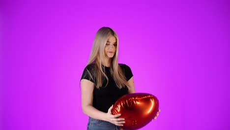 Cute-blonde-woman-hugs-a-red-balloon-heart-and-throws-it-in-the-air,-studio-shot