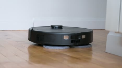 An-autonomous-robot-vacuum-cleaner-spins,-mops,-and-cleans-a-hardwood-floor-in-a-home-living-room