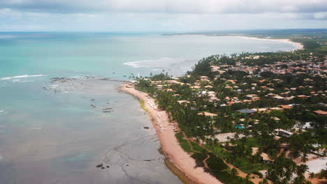 Aerial-view-of-Praia-do-Forte-beach,-the-coral-reef,-palm-tree-area-and-the-city-around,-on-a-cloudy-day,-Praia-do-Forte,-Bahia,-Brazil