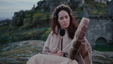 Mujer-Espiritual-Tocando-Pacíficamente-Un-Tambor-Chamánico-En-Un-Hermoso-Pueblo-Medieval-Plano-Medio