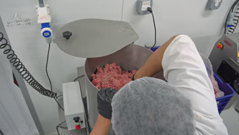 Over-the-shoulder-shot-of-a-man-filling-an-industrial-mincer-with-raw-meat