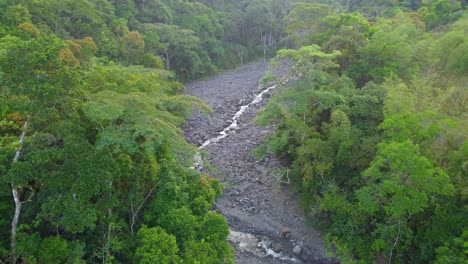 Rio-Negro-trickling-waterway-between-dark-rocks-in-clearing-of-dense-tropical-forest-Risaralda-Colombia,-aerial-establish