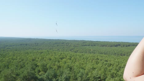 A-woman-admires-the-panoramic-view-of-the-lush-green-forest-and-the-sea-from-the-top-of-the-Stilo-lighthouse-in-Stilo,-Poland-,while-birds-fly-around