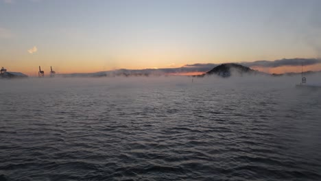 Mist-Rising-From-Water-Near-Bjorvika,-Oslo-With-Golden-Hour-Sunset-On-Horizon
