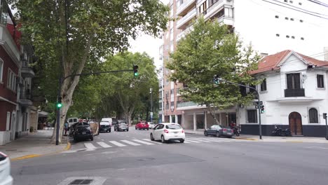 Streets-of-Buenos-Aires-City-Argentina-Flores-Neighborhood,-Cars-Drive-By-Avenue-Asphalted-Urban-Area,-Summer-at-South-American-Capital,-trees-and-traffic-lights