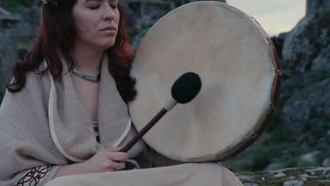 spiritual-woman-peacefully-playing-a-shamanic-drum-in-a-beautiful-medieval-village-medium-close-detail-shot