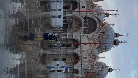 Woman-walks-towards-son-during-Aqua-Alta-to-capture-photos-in-Piazza-San-Marco,-Venice