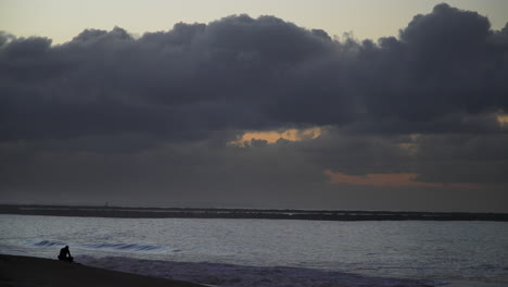 Lone-person-on-Seal-Beach-at-dusk-with-heavy-clouds-over-horizon,-tranquil-ocean-scene