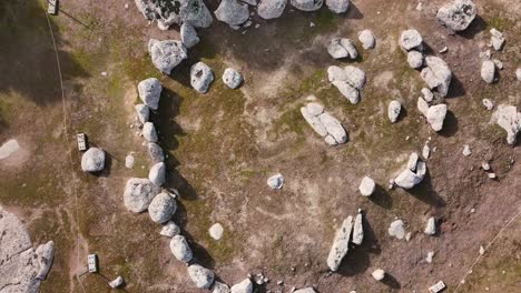 flight-with-a-drone-in-ascent-with-a-top-down-view-and-at-the-same-time-making-a-turn-visualizing-a-stone-cromlech-on-a-brown-ground-with-a-circular-shape-secured-with-a-rope-in-Toledo-Spain