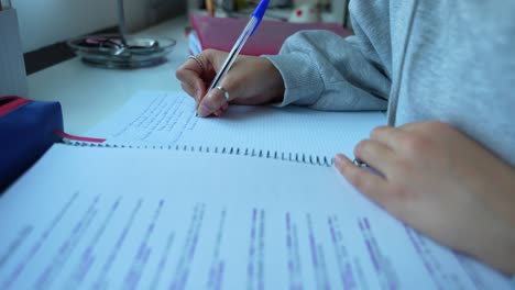 Dedicated-girl-studying-and-making-notes-by-hand-on-table