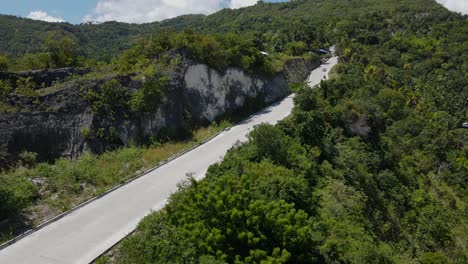 A-motorcycle-riding-on-a-rural-road-in-cebu-island,-lush-greenery-on-sides,-aerial-view