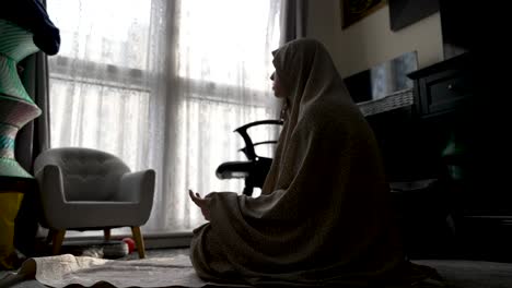 Silhouetted-Muslim-woman-praying-in-a-room,-light-filtering-through-curtains,-reflective-mood