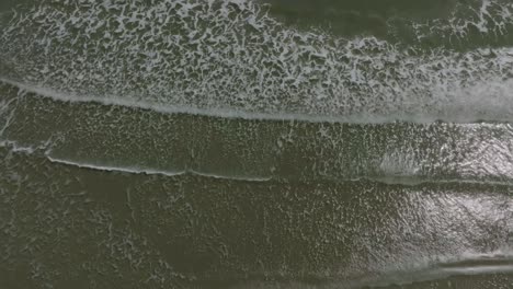 An-aerial,-top-down-view-of-ocean-waves-gently-lapping-up-on-the-beach-of-Galveston-Island,-Texas