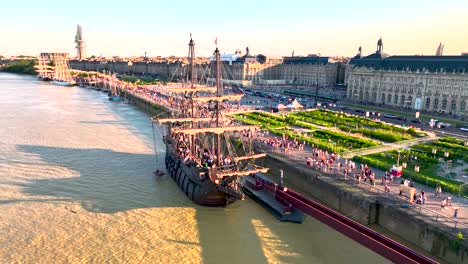 Large-Galleon-sailing-ship-in-the-Garonne-river-during-yearly-Wine-Fair-with-crowded-shore,-Aerial-flyover-shot