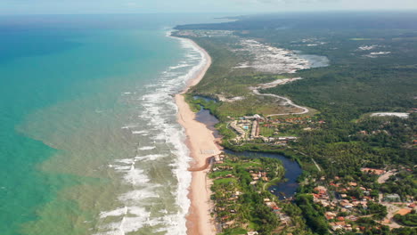 Aerial-view-of-the-waves,-beach,-a-small-river-and-the-palm-trees-area-in-a-cloudy-day,-Imbassai,-Bahia,-Brazil