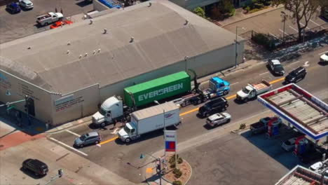 A-green-evergreen-truck-being-towed-in-urban-area,-daylight,-aerial-view