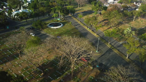Drone-passing-the-Manila-memorial-park-fountain,-in-sunny-Parañaque,-Philippines