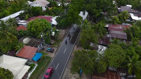 Cars-driving-through-tropical-oslob,-cebu-island-with-lush-greenery,-aerial-view
