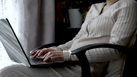 Manos-De-Una-Persona-Femenina-Escribiendo-En-Una-Computadora-Portátil,-Sentada-Al-Lado-De-Las-Cortinas