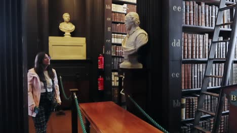 Young-woman-explores-the-ground-level-nooks-at-Trinity-College's-Old-Library-Long-Room,-Dublin