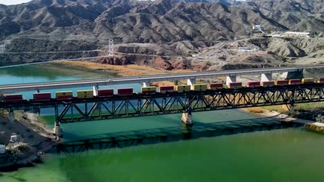 Güterzug,-überquert-Stahlbrücke-über-Den-Colorado-River,-Die-Grenze-Zwischen-Kalifornien-Und-Arizona,-Autobahn-I-40-Ost,-Weitwinkel-Rotationsflug-Mit-Drohne