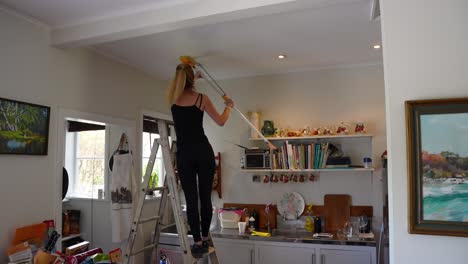 Blonde-woman-stands-on-the-kitchen-stairs-in-a-living-room-cleaning-the-ceiling