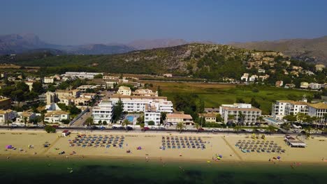 Playa-del-port-de-pollenca-with-sunbathers-and-parasols,-mallorca,-spain,-on-a-sunny-day,-aerial-view