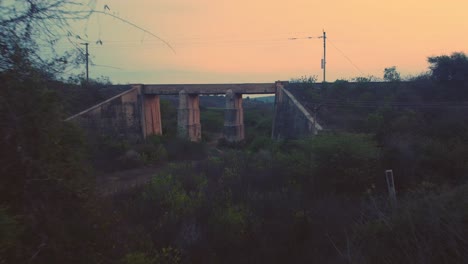 Luftaufnahme-Einer-Verlassenen-Alten-Eisenbahnbrücke-Aus-Beton-Mit-Dichten-Waldhügeln-Im-Hintergrund-Während-Der-Späten-Abendzeit