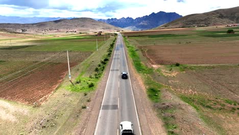 Experience-the-thrill-of-traversing-the-winding-roads-of-the-Bolivian-high-altitude-Andes-as-a-car-is-followed,-with-majestic-mountains-as-the-backdrop-and-vibrant-farms-lining-the-roadside
