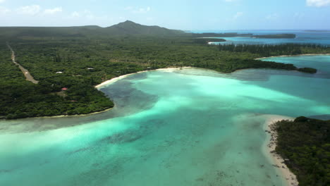 Isle-of-Pines,-New-Caledonia-lagoon,-beach-and-distant-N'Ga-peak-on-the-island's-columnar-pine-forest---aerial-forward