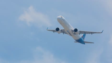 Large-plane-rises-quickly-up-into-air-with-blue-striping-along-tail-against-white-cloudy-sky