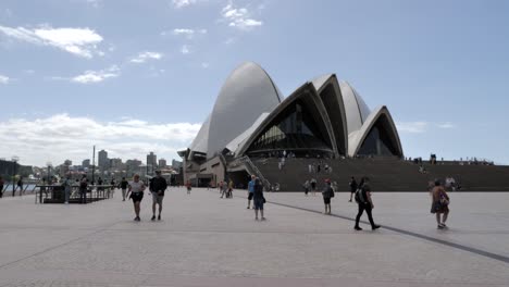 Tourists-and-locals-walk-around-iconic-Sydney-Opera-house-on-bright-sunny-day,-New-South-Wales,-Australia