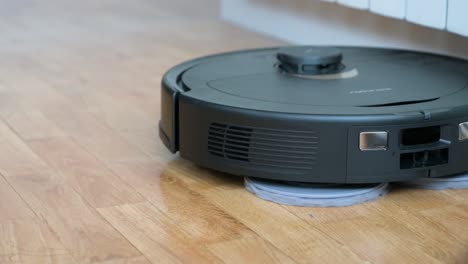 An-autonomous-robot-vacuum-cleaner-spins-and-cleans-a-hardwood-floor-in-a-home-living-room