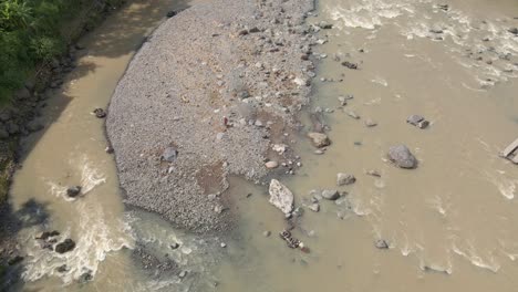 A-man-carries-river-stones-using-a-floating-tub-and-passes-through-the-river-flow