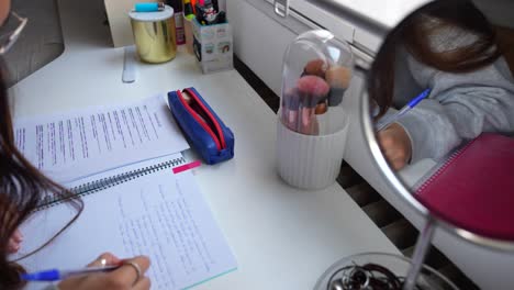 Close-up-pan-shot-of-a-study-desk-with-writing-materials-and-makeup-brushes-while-woman-hands-writes