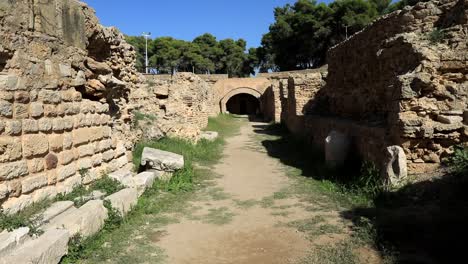Sunny-day-at-the-ancient-Roman-ruins-in-Carthage,-Tunisia,-with-a-clear-blue-sky-and-historical-arches